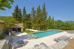 A swimming pool with lounge chairs, a stone building, and a forested hillside.