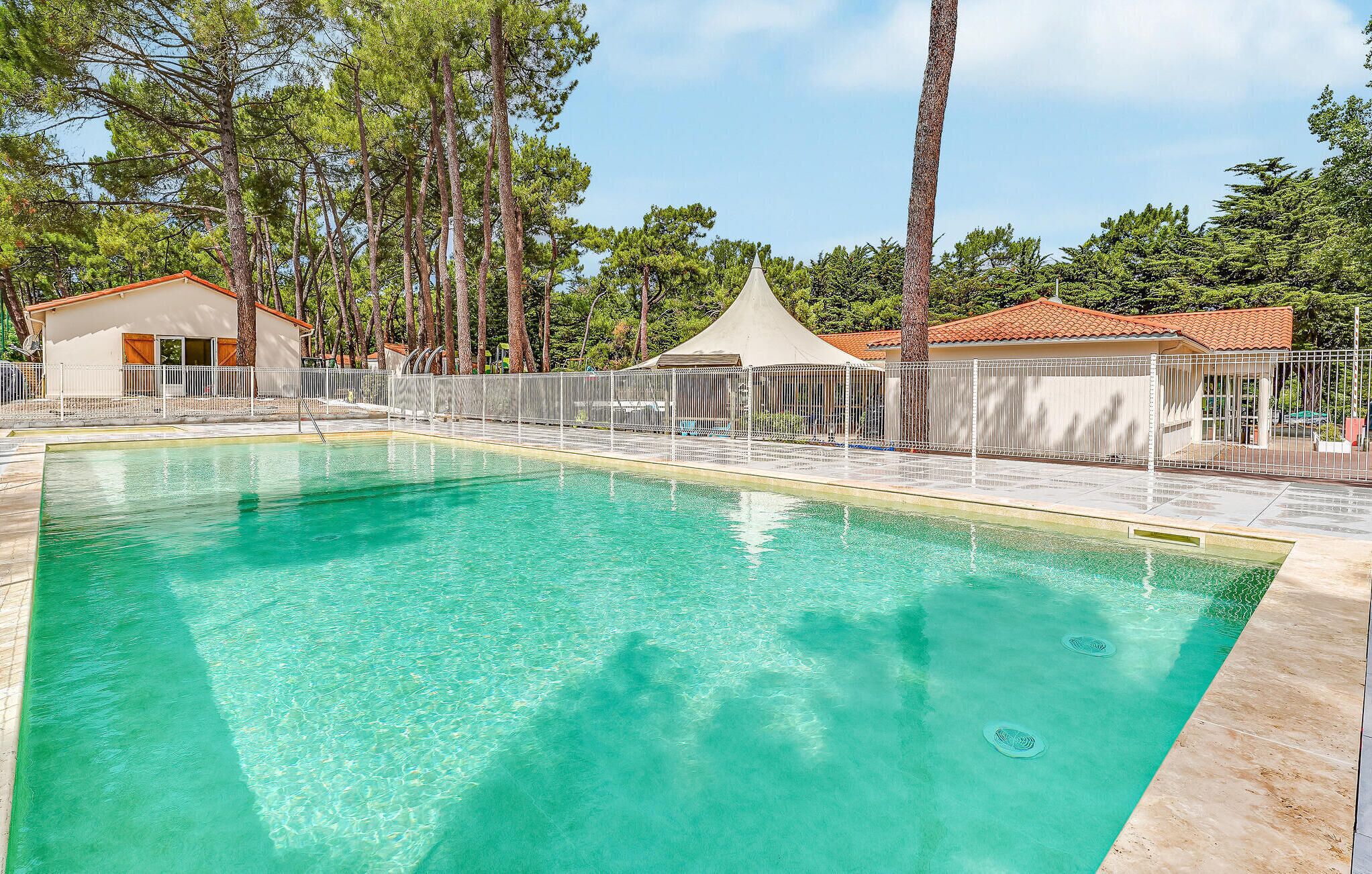 A clear swimming pool with a tiled deck, surrounded by a white fence and trees.