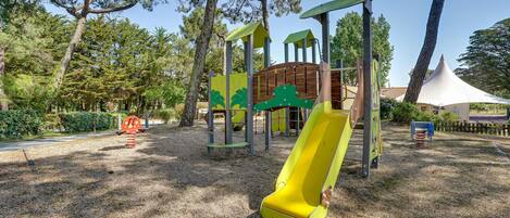 A playground with a yellow slide, climbing structures, and a wooden playhouse.