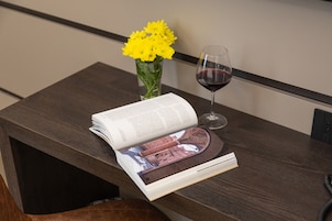 Un tavolo in legno con un libro, un bicchiere di vino rosso e un vaso di fiori gialli.