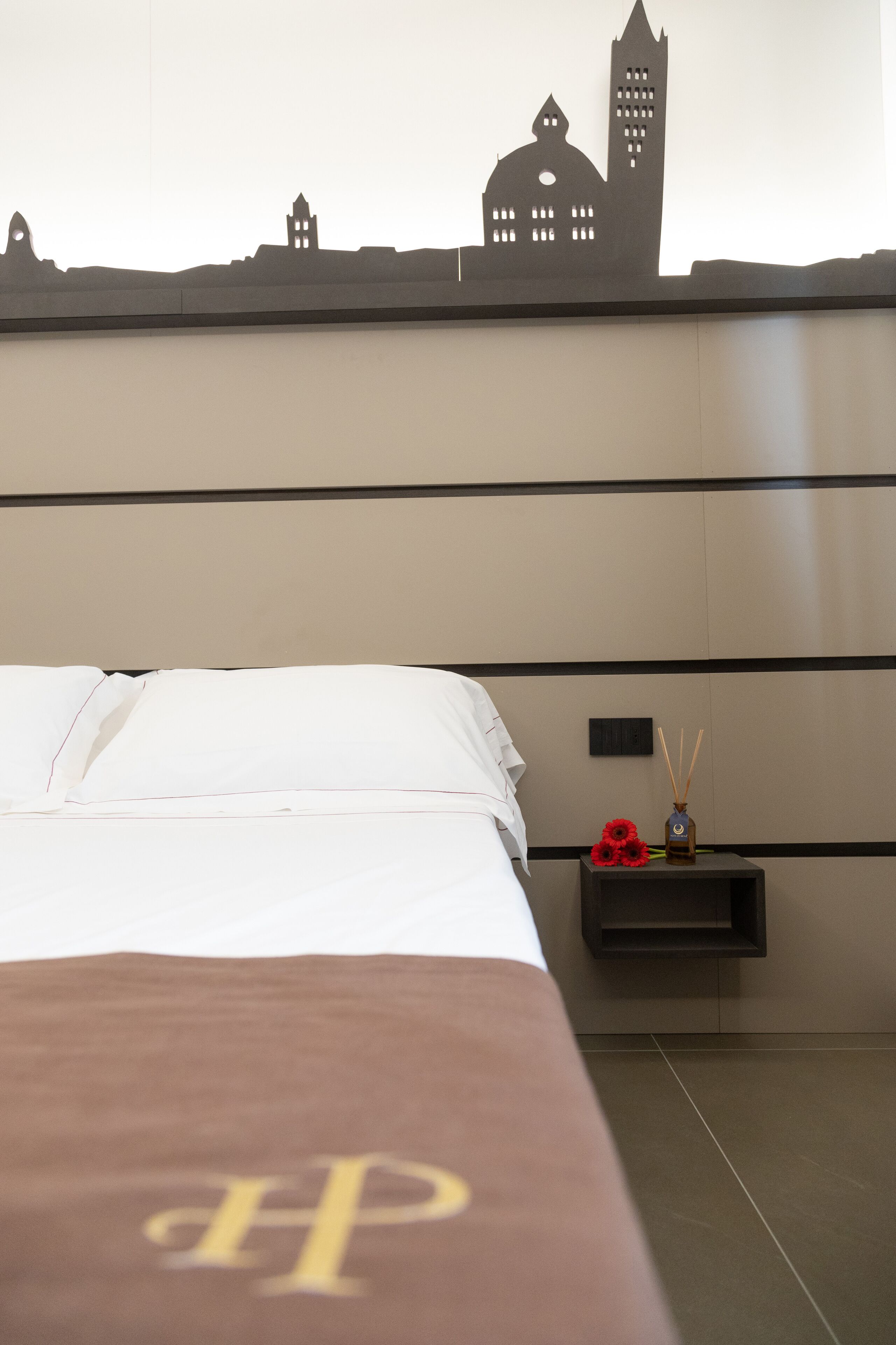 Ein Hotelzimmer mit Bett, Nachttisch und Wanddeko einer Stadtansicht.