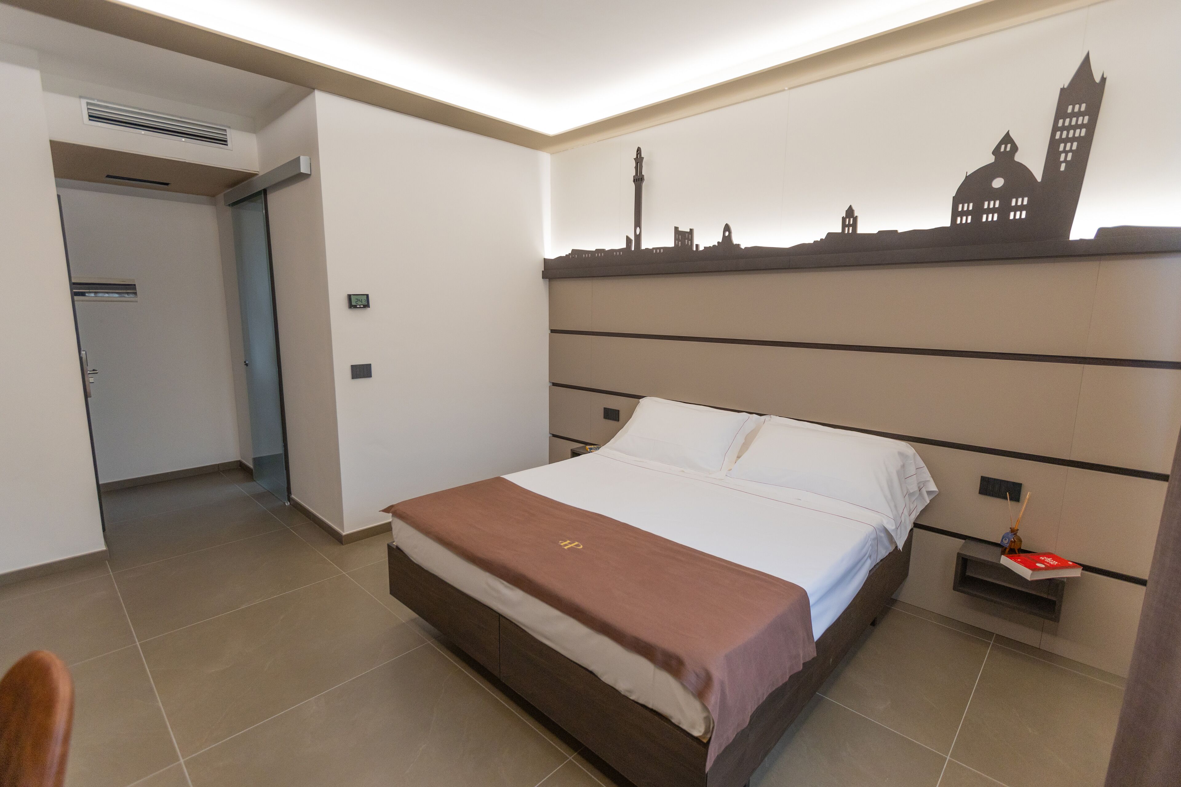 A hotel room with a bed, a city skyline mural, a nightstand, and a door leading to another room.