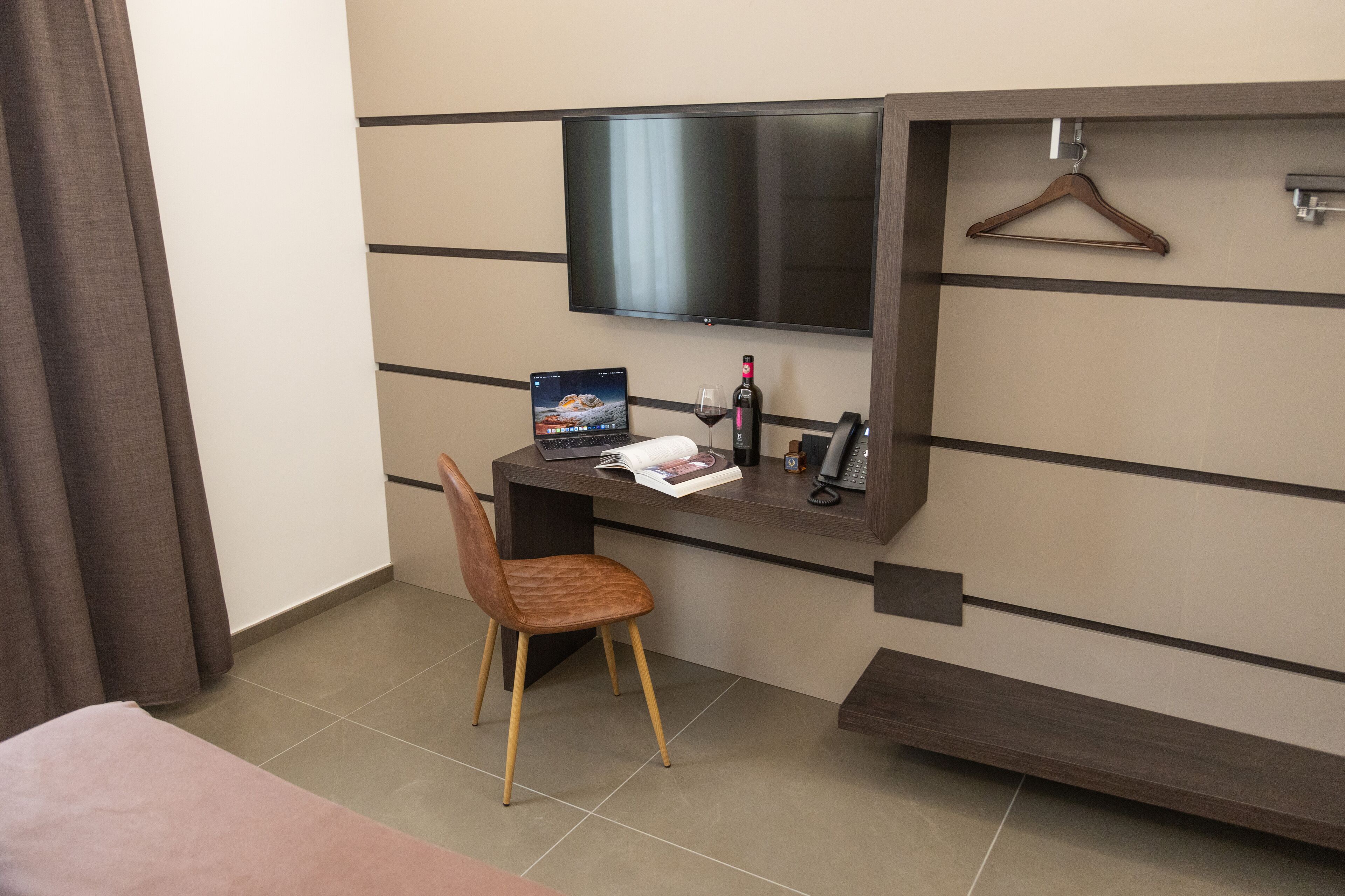 Une chambre d’hôtel avec un lit, un bureau avec un ordinateur portable, une chaise, un téléviseur fixé au mur et un verre à vin.