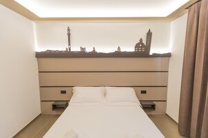 Una camera d'albergo con un letto, una testiera che raffigura la sagoma di un orizzonte cittadino, un comodino e una tenda sulla destra.