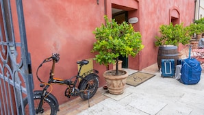 Een rood gebouw met een receptiebord, een fiets, bloempotten en bagage.