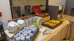 Een buffetopstelling met diverse gerechten, waaronder yoghurtbekers, fruit en een schaal druiven.
