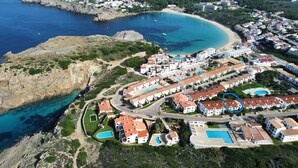 An aerial view of a coastal resort with multiple buildings, swimming pools, and a beach.