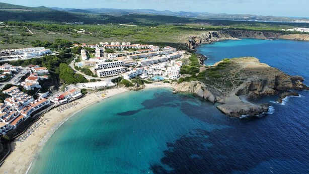 An aerial view of a coastal resort with multiple buildings, a beach, and a rocky coastline.