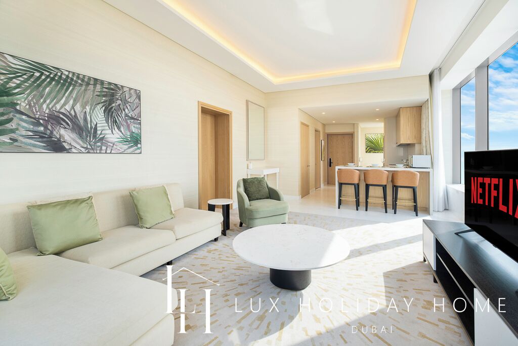 Un salon moderne avec un canapé, une table basse et des œuvres d’art. On aperçoit à l’arrière-plan un coin cuisine avec une table et des chaises.