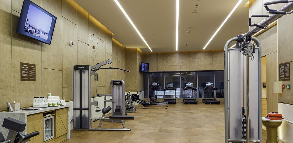 A gym with cardio machines, weight training equipment, a TV on the wall, and a wooden floor.