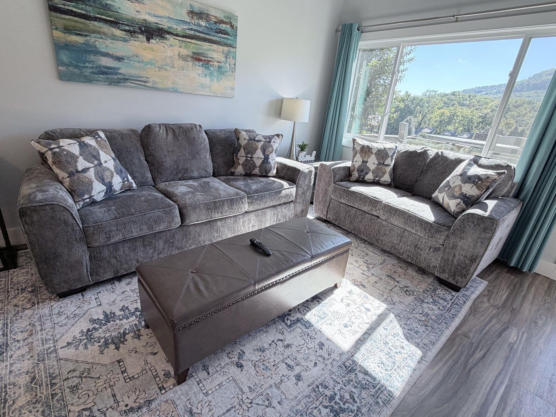 A living room with a grey sofa set, a brown ottoman, and a patterned rug.