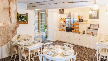 Un comedor con mesas y sillas blancas, una cocina con armarios blancos y un suelo estampado.
