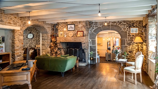 A cozy room with a stone fireplace, wooden furniture, and a green sofa. - Demeures & Châteaux - Hôtel de la porte Saint-Malo - DINAN (Dinan)
