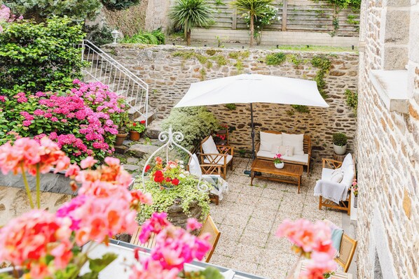 A stone patio with outdoor furniture, a white umbrella, and flowering plants. - Demeures & Châteaux - Hôtel de la porte Saint-Malo - DINAN (Dinan)