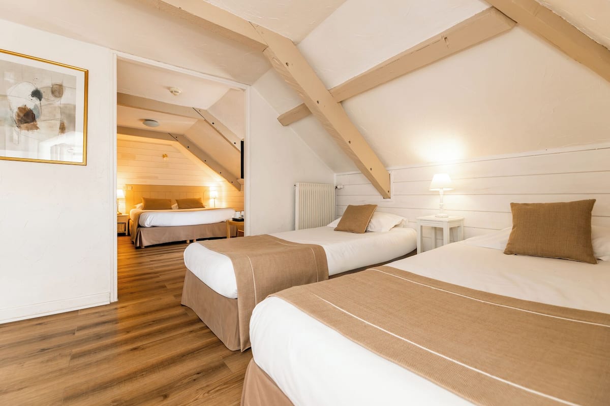 A cozy attic bedroom with two beds, wooden beams, and a framed picture on the wall.