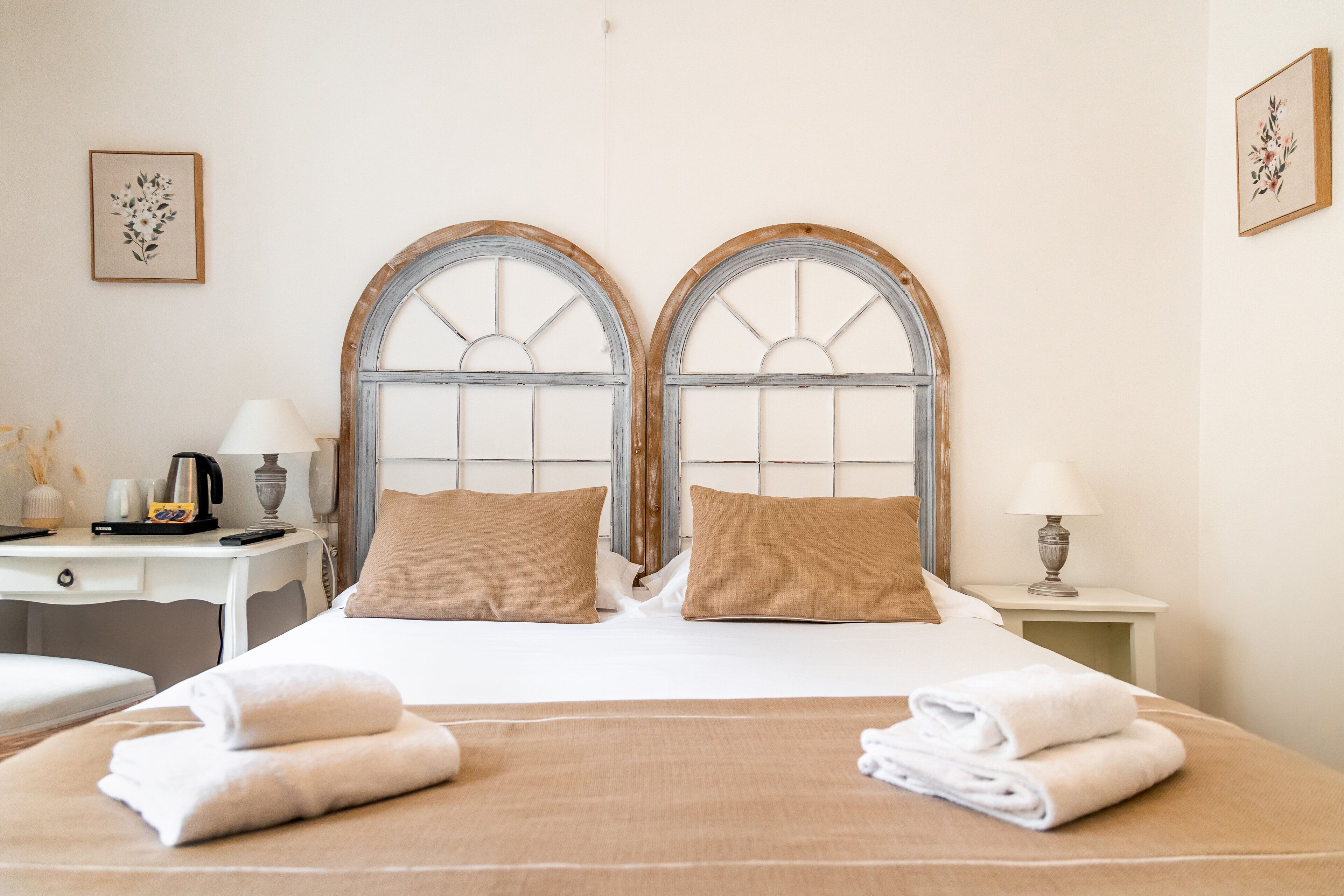 A hotel room with a large bed, two pillows, a desk with a lamp, and a nightstand with a lamp.