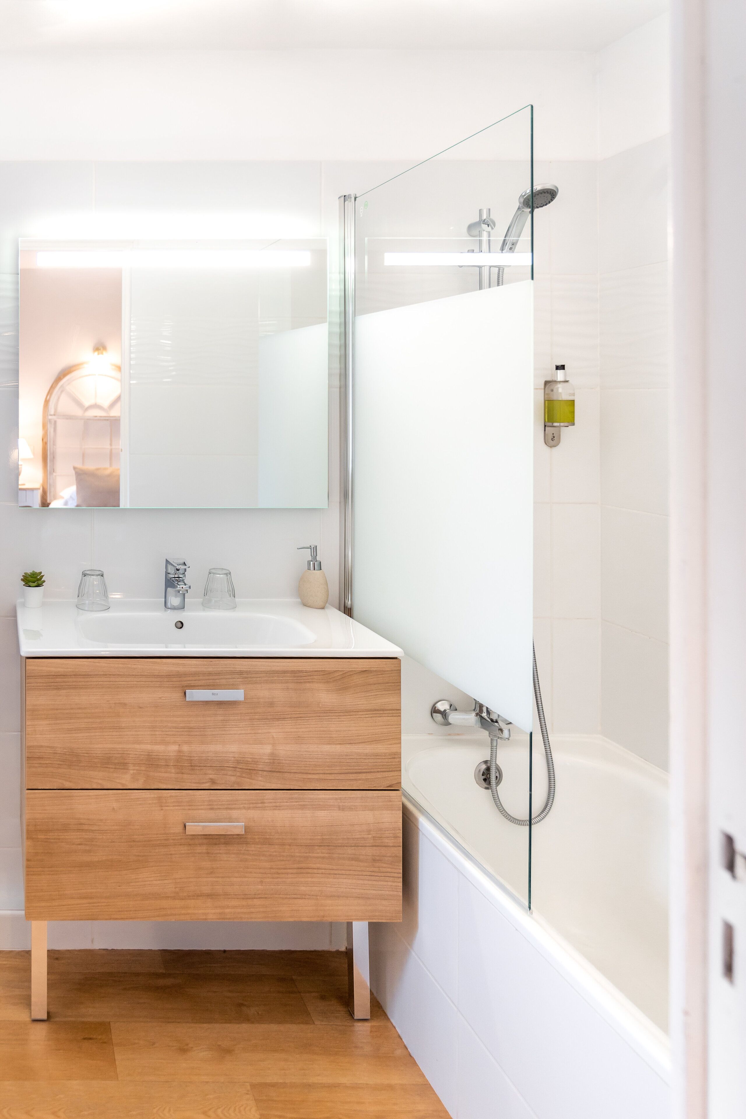 A modern bathroom with a wooden vanity, a glass shower enclosure, and a white tiled wall.