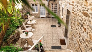 A stone courtyard with outdoor seating and a view of a stone building. - Demeures & Châteaux - Hôtel de la porte Saint-Malo - DINAN (Dinan)