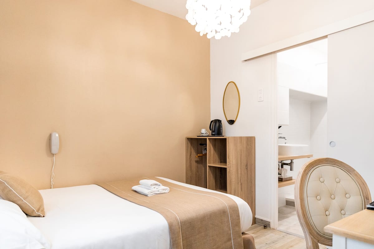 A hotel room with a bed, a wooden wardrobe, a chair, a desk, and a mirror.