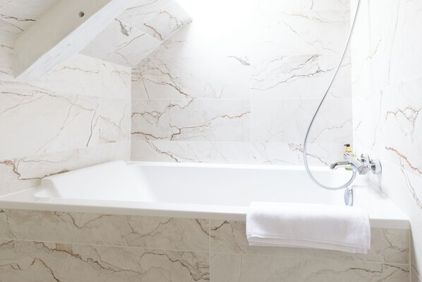 Un baño con pared y suelo de mármol, una bañera blanca y una toalla colgada a un lado.