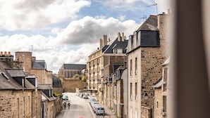 A narrow street lined with stone buildings, a cyclist, parked cars, and a balcony with flowers. - Demeures & Châteaux - Hôtel de la porte Saint-Malo - DINAN (Dinan)