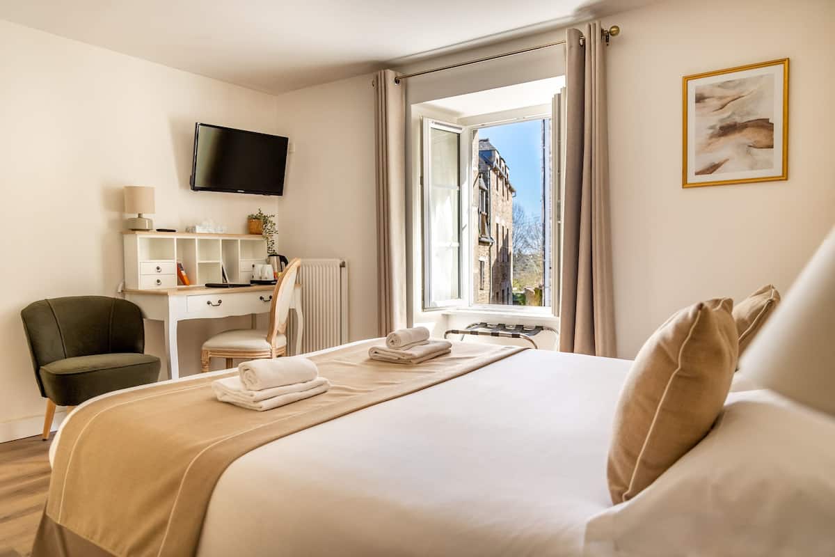 A hotel room with a bed, a desk, a chair, a television, and a window with curtains.