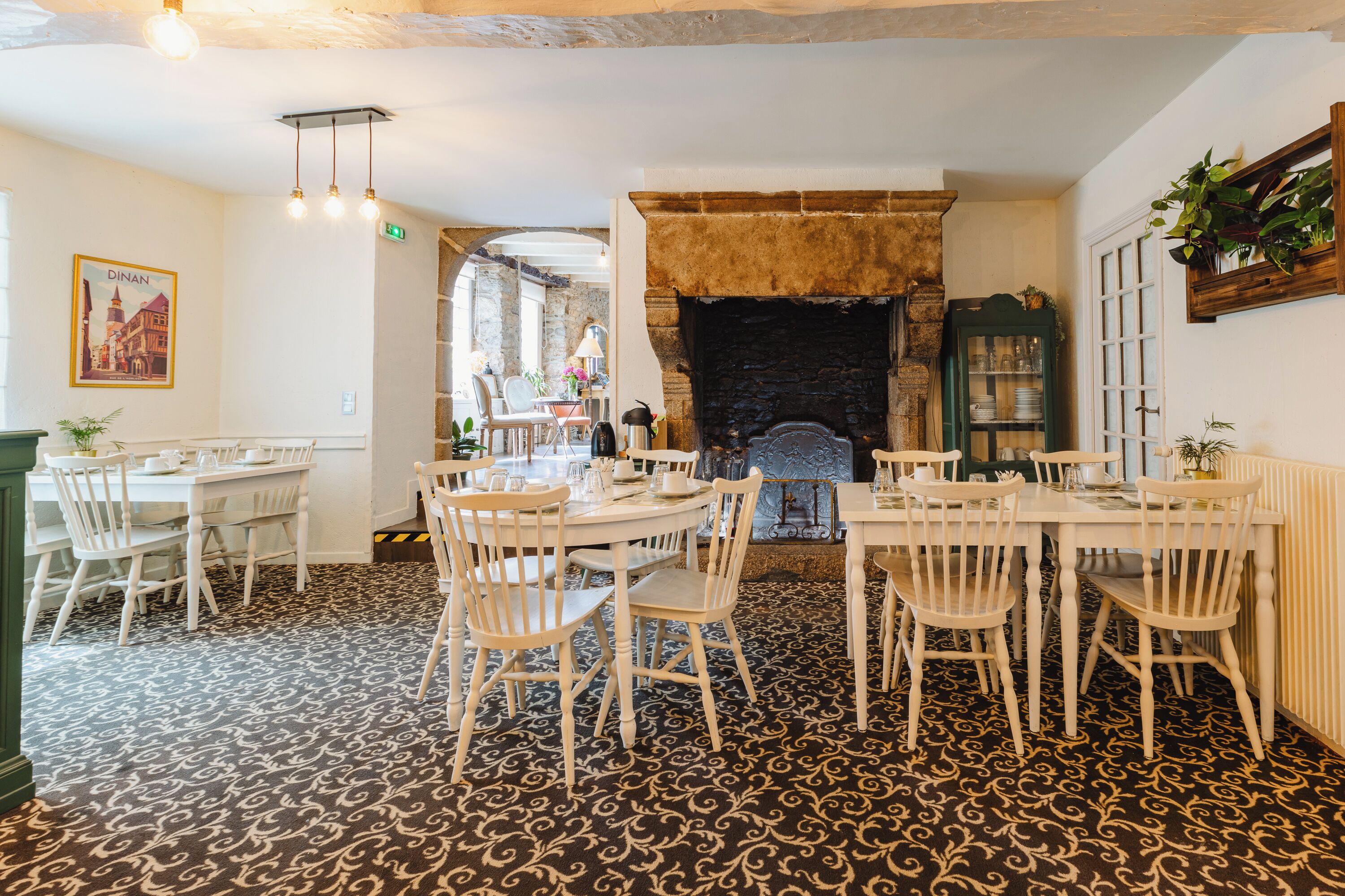 A dining area with white tables and chairs, a patterned carpet, and a fireplace.