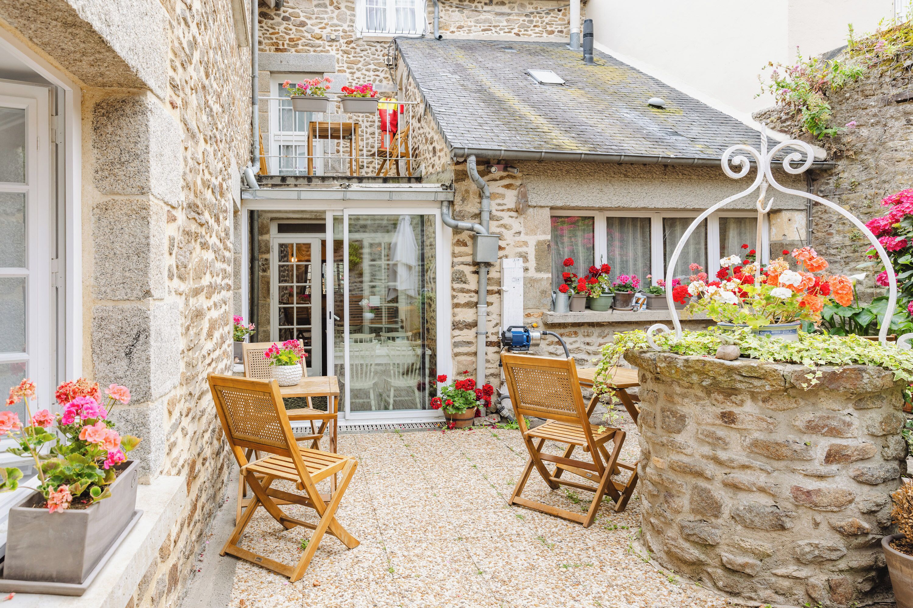 A stone building with a balcony, a table with chairs, and potted plants.