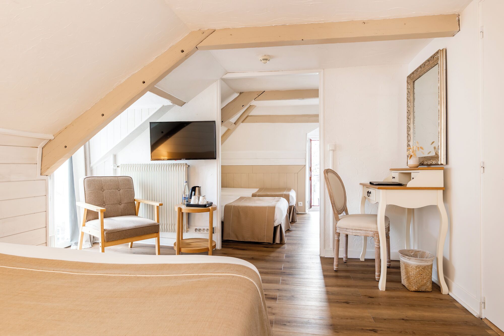 A cozy attic bedroom with a wooden ceiling, a TV, a desk with a chair, and a bed.