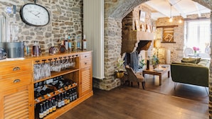 A stone-walled bar area with a clock, wine bottles, glasses, and a rustic fireplace. - Demeures & Châteaux - Hôtel de la porte Saint-Malo - DINAN (Dinan)
