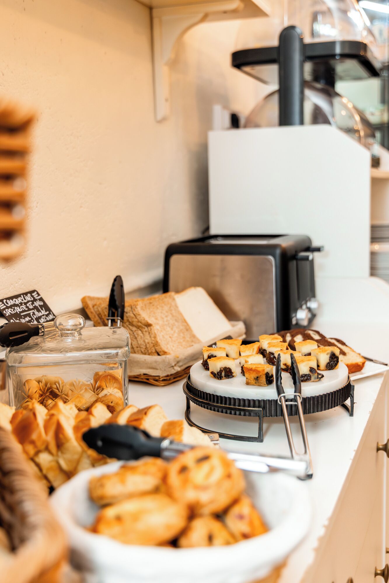 A buffet with various pastries, a coffee machine, and a sign indicating breakfast options.