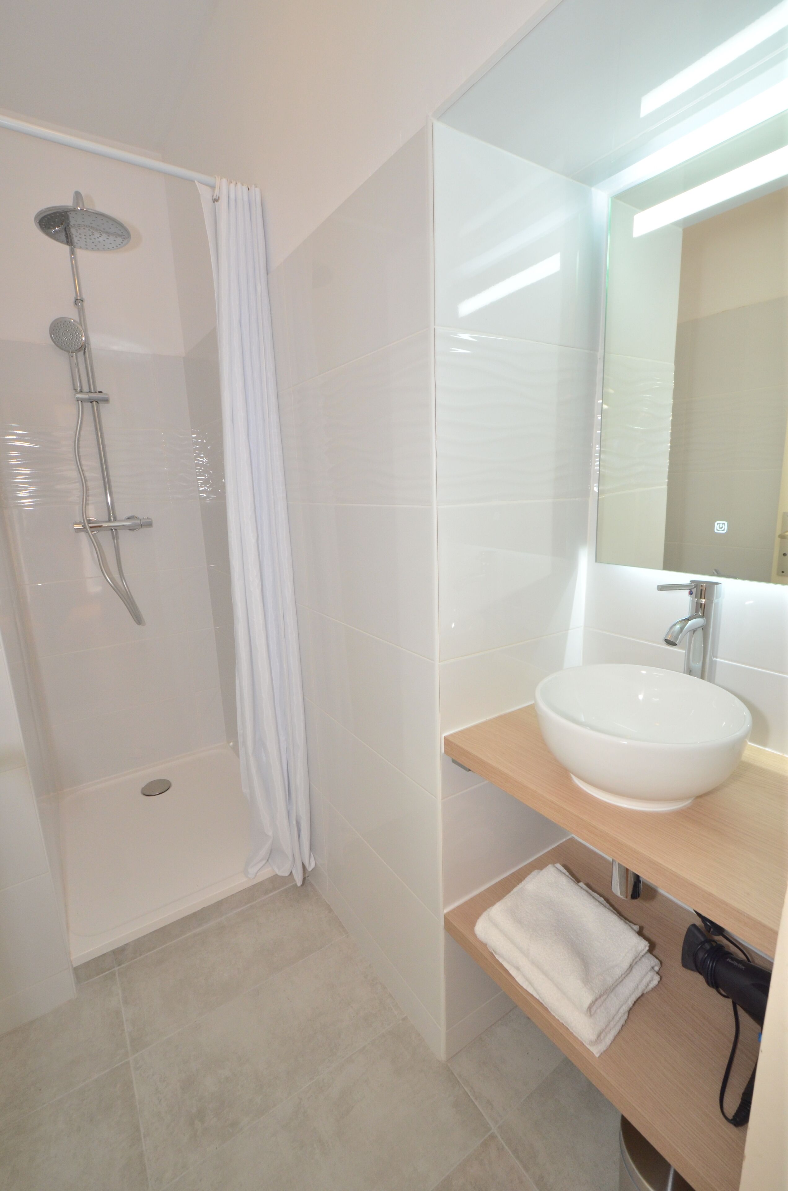 A modern bathroom with a glass shower enclosure, a white sink, and a mirror above it.