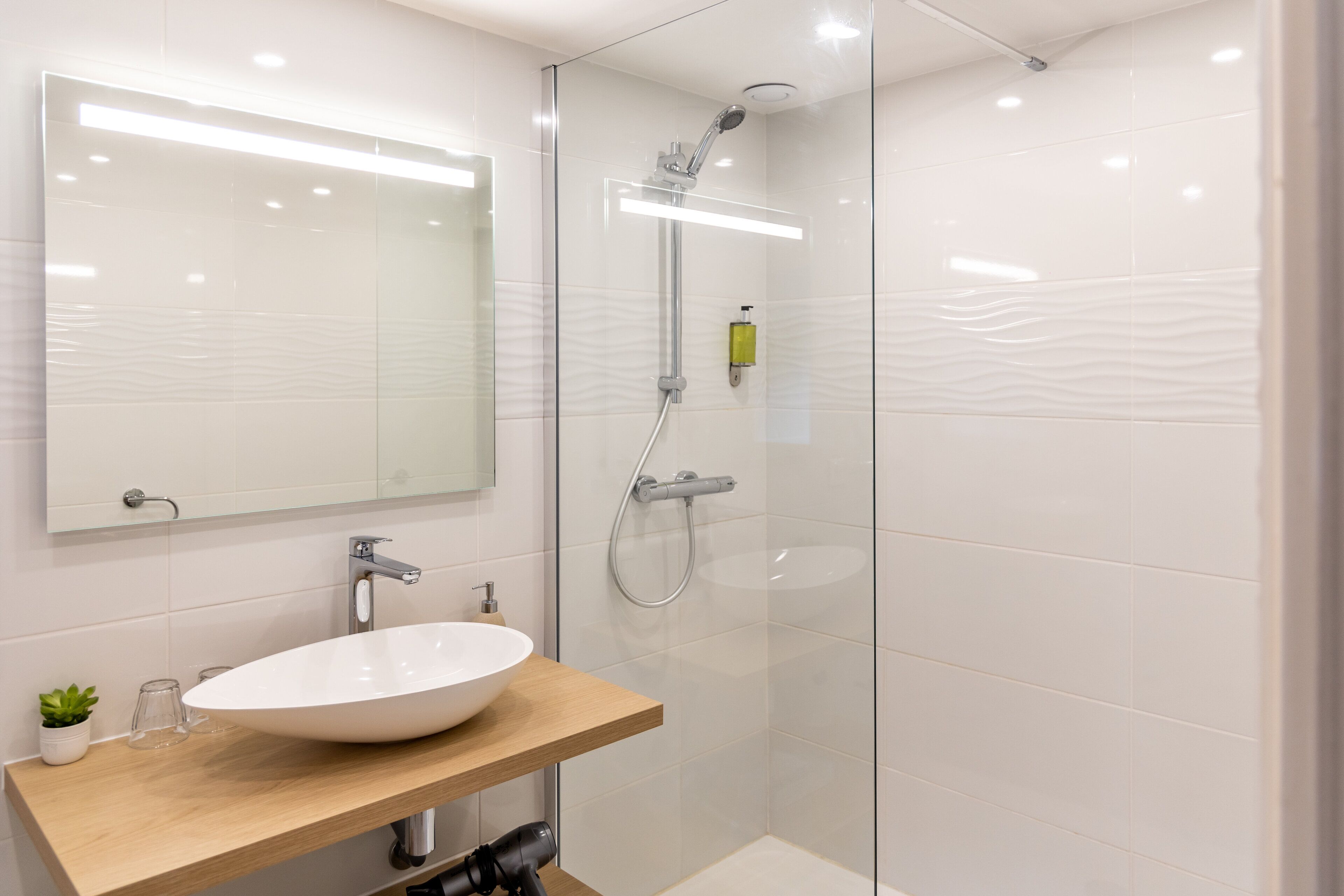 A modern bathroom with a white sink, a wooden countertop, a large mirror, and a glass-enclosed shower area.
