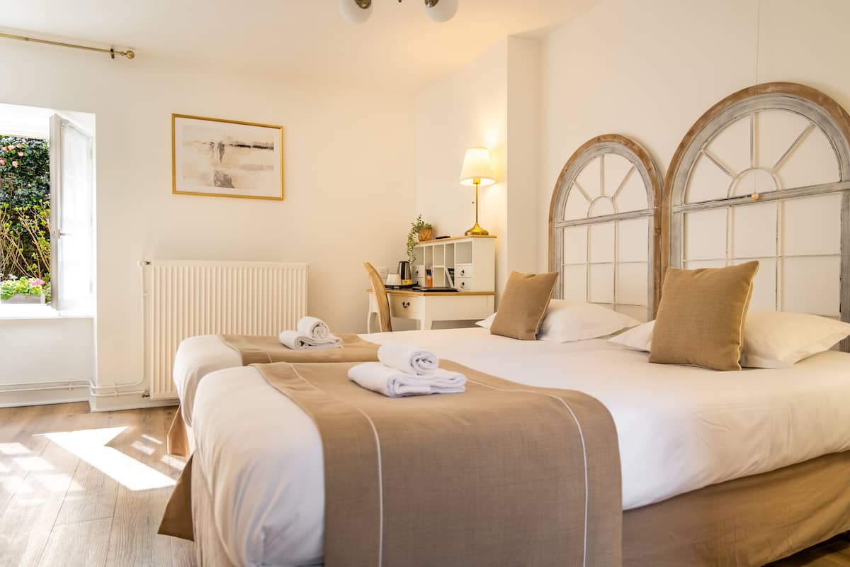 A hotel room with two beds, a desk, a lamp, and a window with a view of greenery.