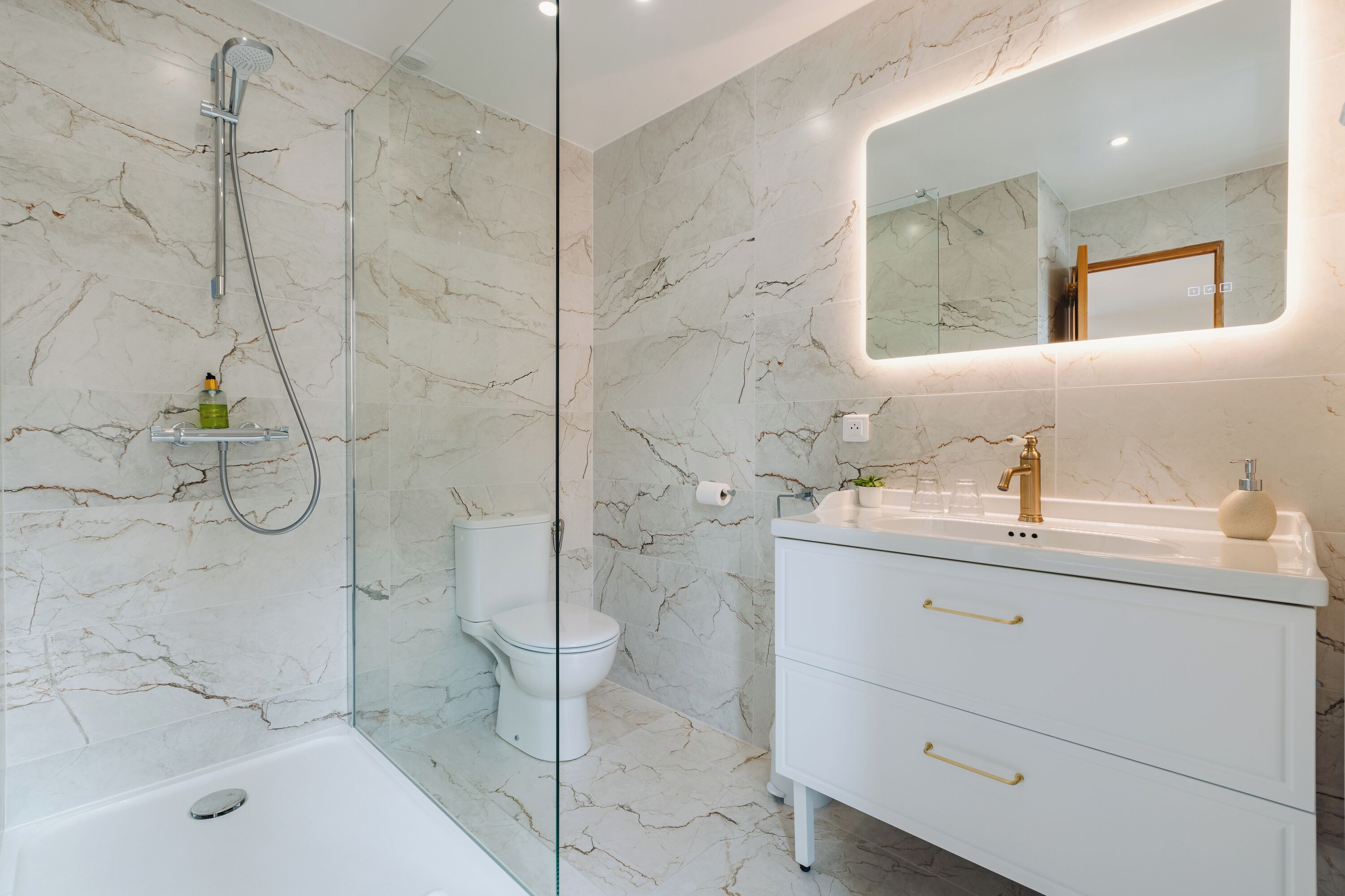 A modern bathroom with a glass-enclosed shower, a white toilet, and a vanity with gold handles.