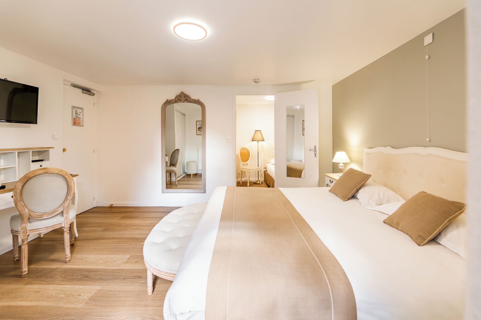 A hotel room with a large bed, a desk with a chair, a television, and a mirror.