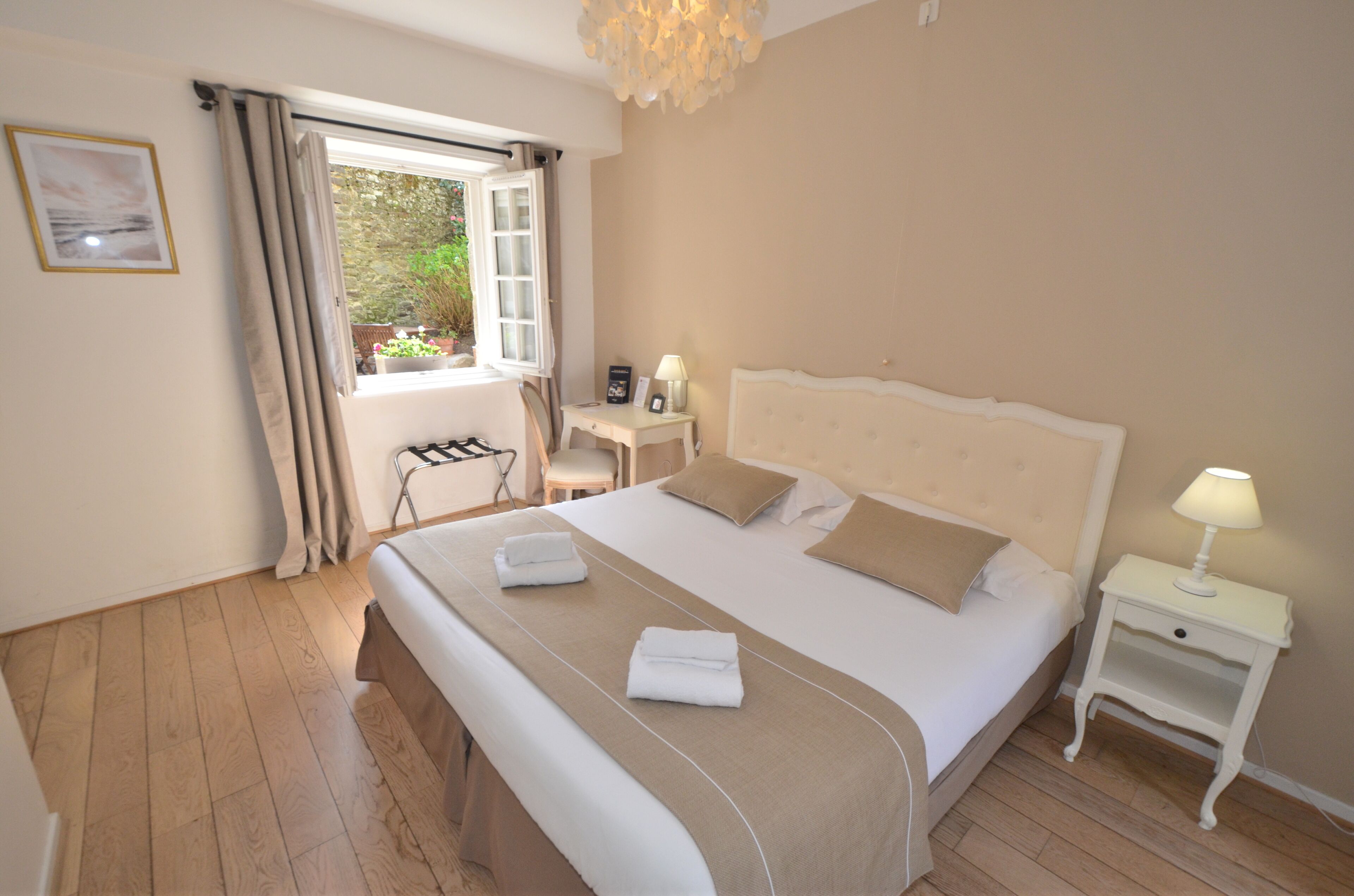 A neatly made bed with a beige headboard, a bedside table with a lamp, and a window with curtains.