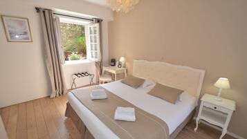 A neatly made bed with a beige headboard, a bedside table with a lamp, and a window with curtains.