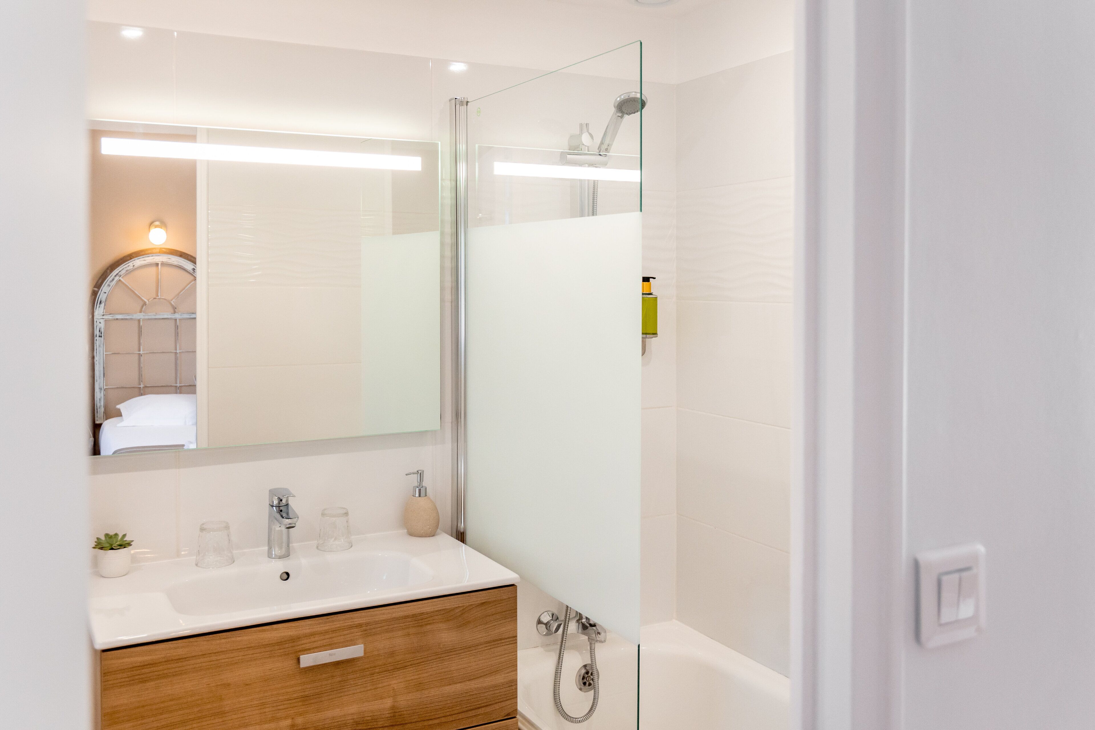 Une salle de bain moderne avec une douche à l’italienne en verre, un meuble-lavabo en bois et un grand miroir.