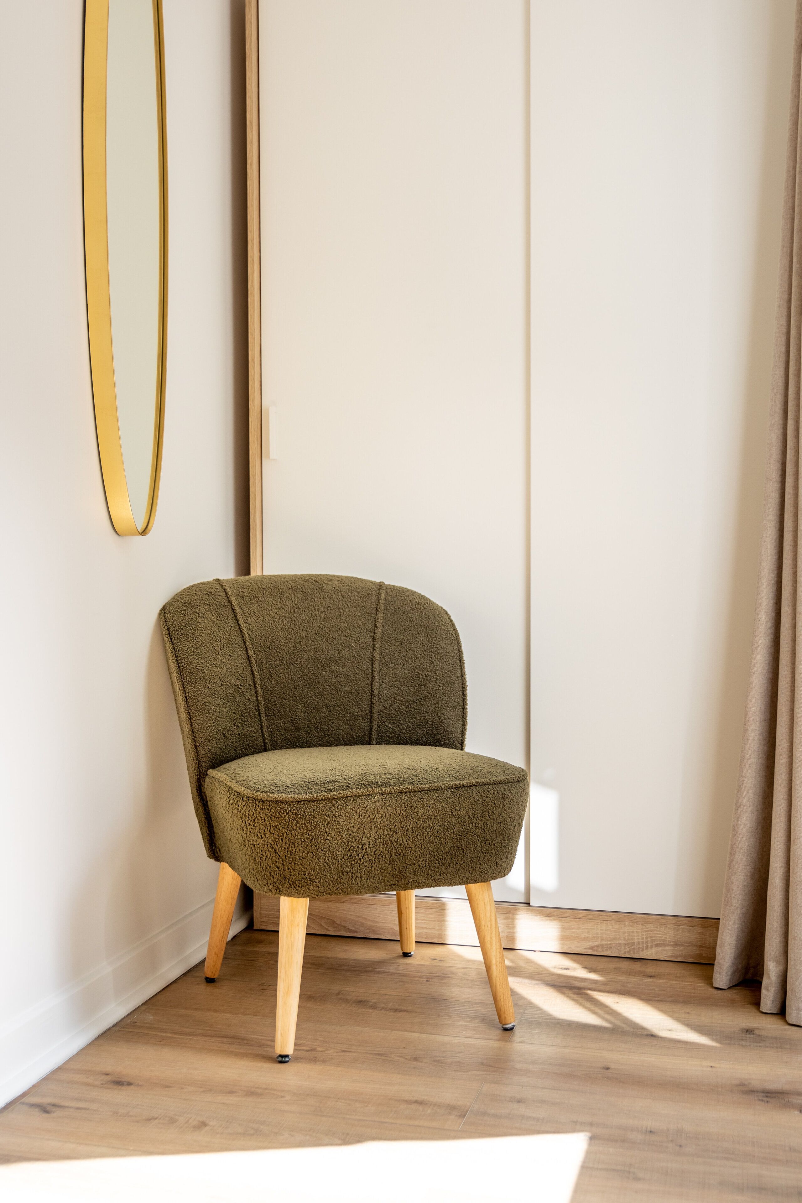 Ein moderner Sessel mit Holzbeinen und Strukturstoff, platziert in einem Raum mit Holzboden und schlichter Wand.