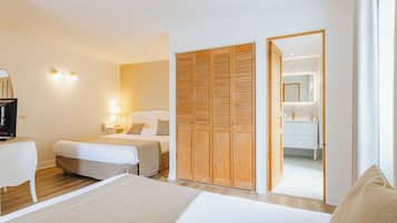 A hotel room with two beds, a desk, a wardrobe, and a bathroom visible through an open door.