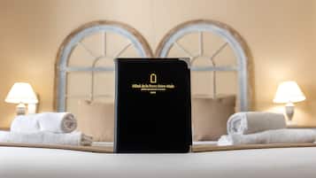 Un livre à couverture noire intitulé « Hôtel de la Porte Saint-Malo » est posé sur un lit, avec des serviettes blanches et deux lampes de chaque côté.