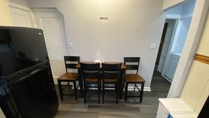 Una cucina compatta con un frigorifero nero, un tavolo da pranzo con quattro sedie e un cartello 'No Smoking' appeso al muro.