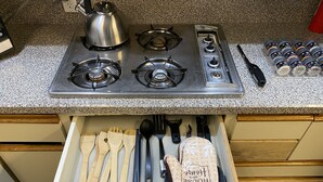 Una cucina con piano cottura in acciaio inossidabile, bollitore e un cassetto contenente utensili da cucina in legno e un panno.