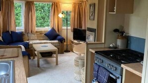 A compact RV kitchen with a stove, sink, and a dining area with a sofa and table. - Cosy, Quiet Static Caravan, Mawgan Porth, St Eval (Wadebridge)