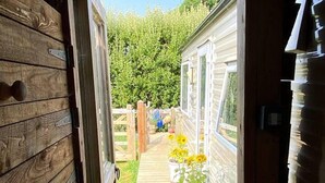 A wooden deck leading to a mobile home with a garden area and potted plants. - Cosy, Quiet Static Caravan, Mawgan Porth, St Eval (Wadebridge)