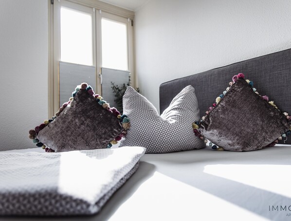 A neatly made bed with a gray headboard and decorative pillows. - Central Apartment with Netflix and a WE 50 Spring Mattress (Magdeburg)