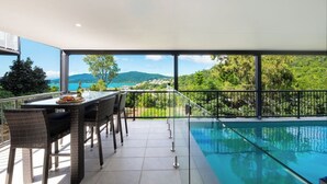 A balcony with a pool, outdoor seating, and a scenic view of mountains and a lake.