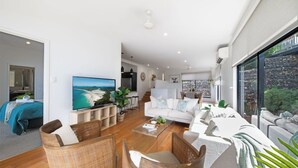 A modern living room with a large flat-screen TV, wicker furniture, and a view of the city through large windows.