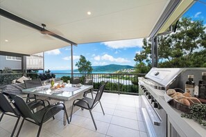 A balcony with a glass table, chairs, and a barbecue grill.